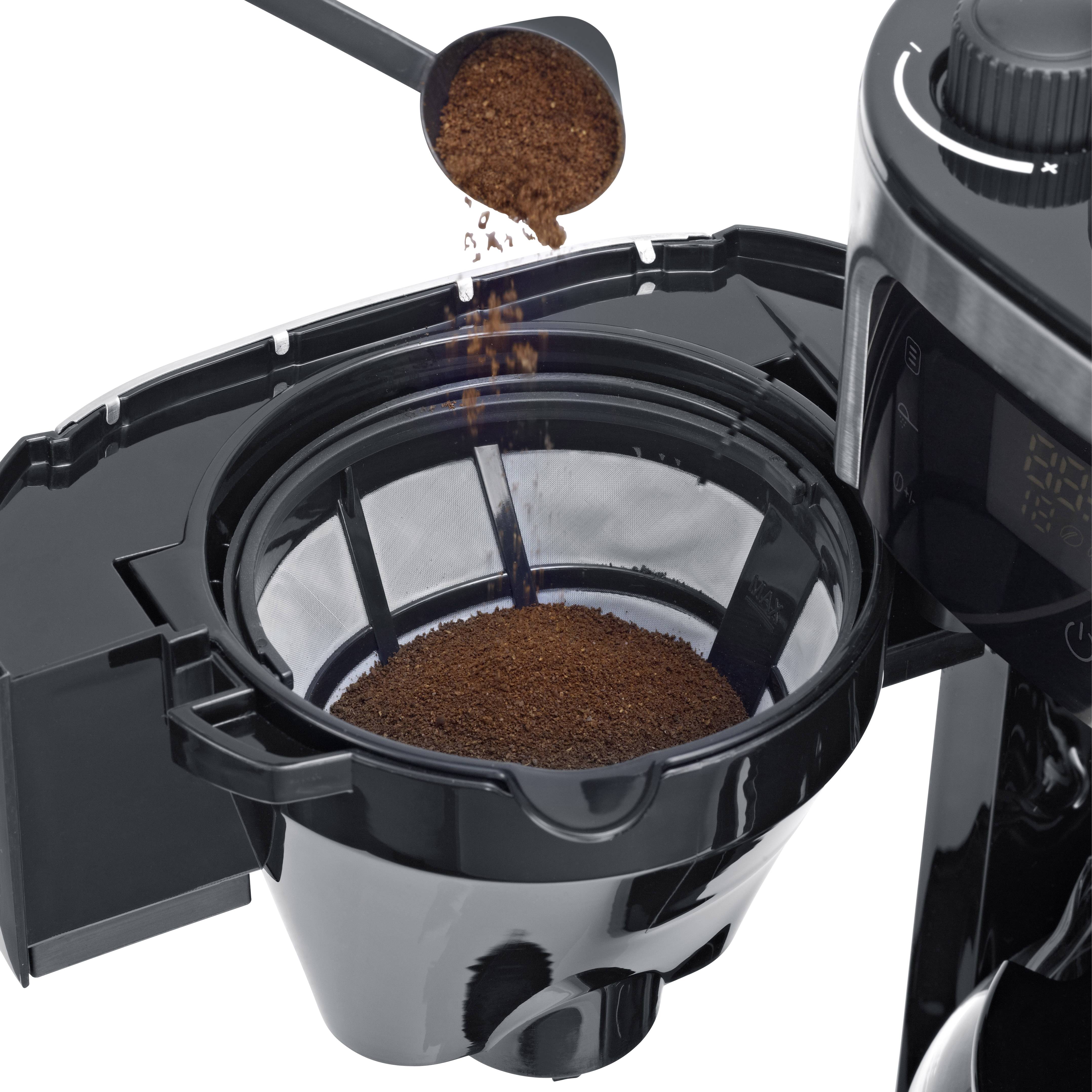 Machine à café avec le porte-filtre ouvert. Une cuillère de café moulu est versée dans le filtre.