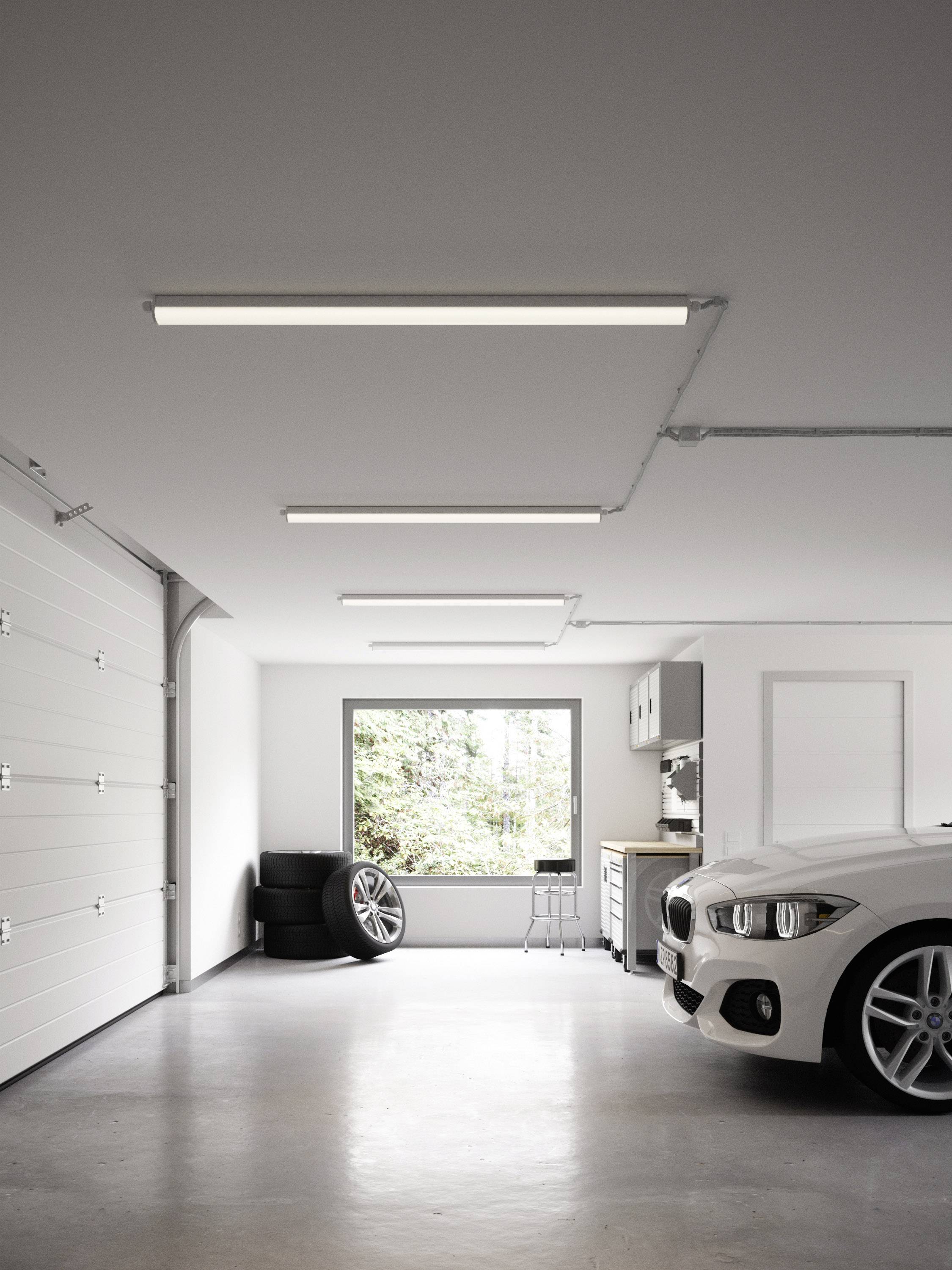 Garage lumineuse et moderne avec une voiture blanche, des pneus empilés dans un coin, et une grande fenêtre offrant une vue sur les arbres à l'extérieur.