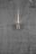 Mur gris avec une fissure, sur lequel est fixée une petite lampe murale ronde diffusant une lumière douce vers le haut.