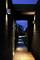 Un sentier étroit et éclairé traverse un corridor couvert en bois sombre. Éclairage extérieur et crépuscule.