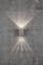 Applique murale en métal projetant des rayons lumineux symétriques, dirigés vers le haut et vers le bas, sur un mur de béton gris.