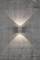 Applique murale sur un mur de béton gris et fissuré, projetant de la lumière vers le haut et le bas et créant un motif en forme de X.