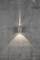 Une lampe moderne sur un mur gris texturé. L'éclairage rayonne vers le haut et vers le bas, créant une lumière douce et diffuse.