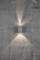 Un applique murale en acier brossé projette deux faisceaux lumineux coniques vers le haut et vers le bas sur un mur gris structuré.