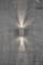 Une applique murale de forme cylindrique diffuse une lumière chaleureuse vers le haut et le bas sur un mur en béton gris aux fines fissures.