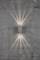 Une lampe murale grise projette des rayons lumineux vers le haut et le bas sur un mur de béton brut et gris.