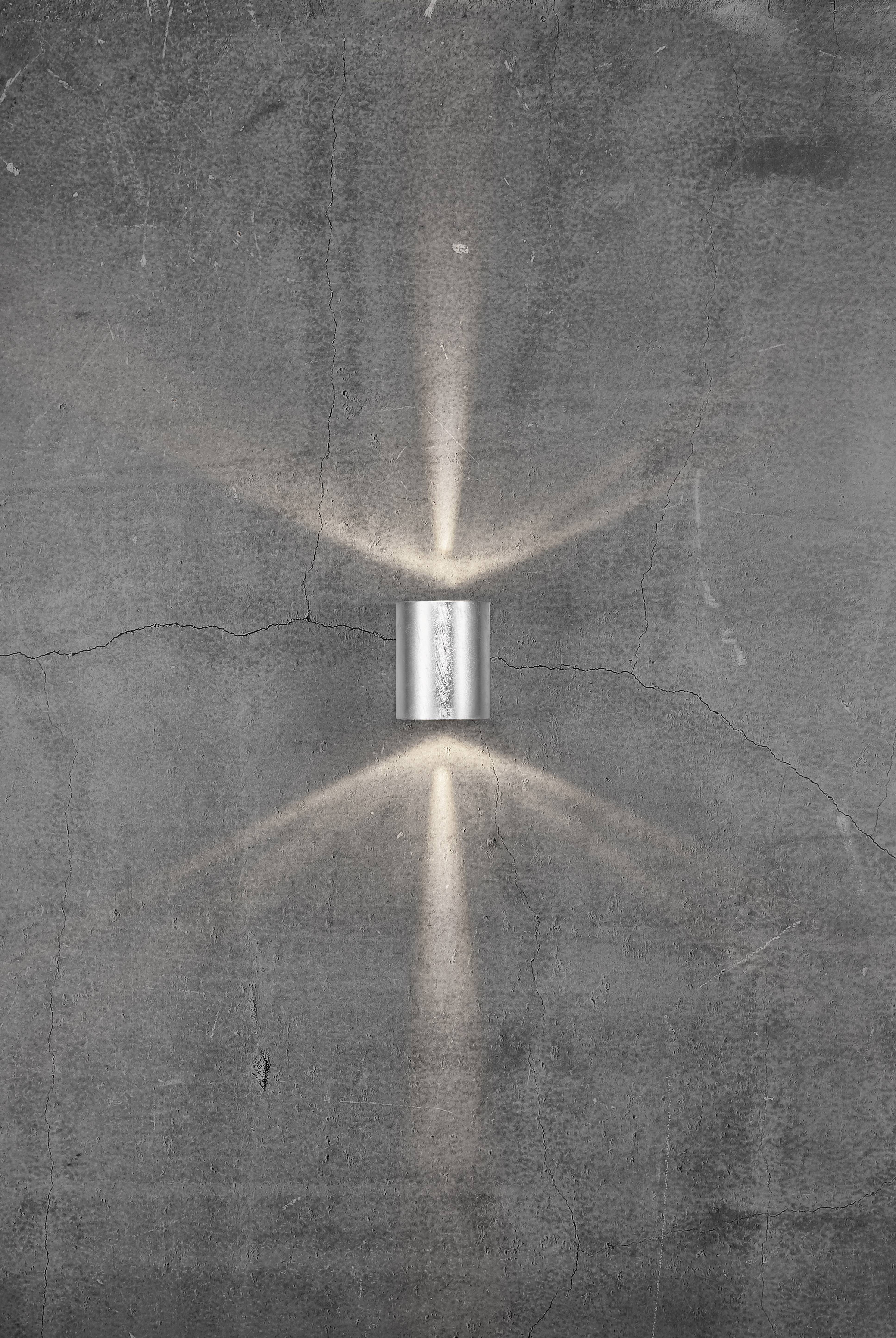 Applique murale sur un mur de béton gris, projetant des rayons lumineux vers le haut et vers le bas, créant une atmosphère décorative.