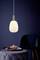 Une lampe suspendue éclaire une table ronde avec un bol et des fleurs. À l'arrière-plan se trouve une chaise bleu foncé.