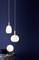 Trois lampes suspendues modernes blanches devant un fond bleu foncé, en dessous une petite table avec des coussins et une lampe de table ronde.