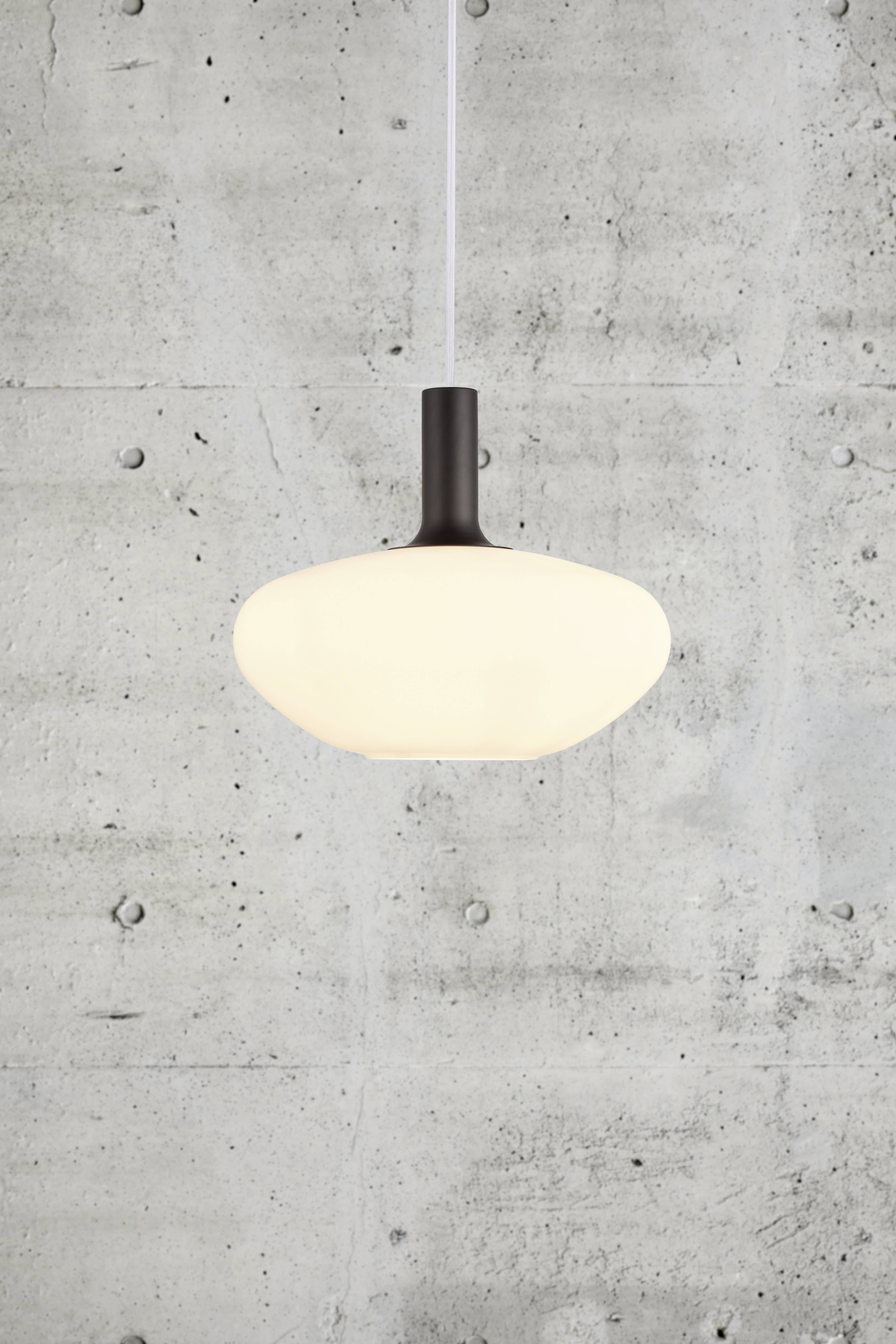 Suspension lumineuse avec un abat-jour clair et ovale devant un mur en béton.