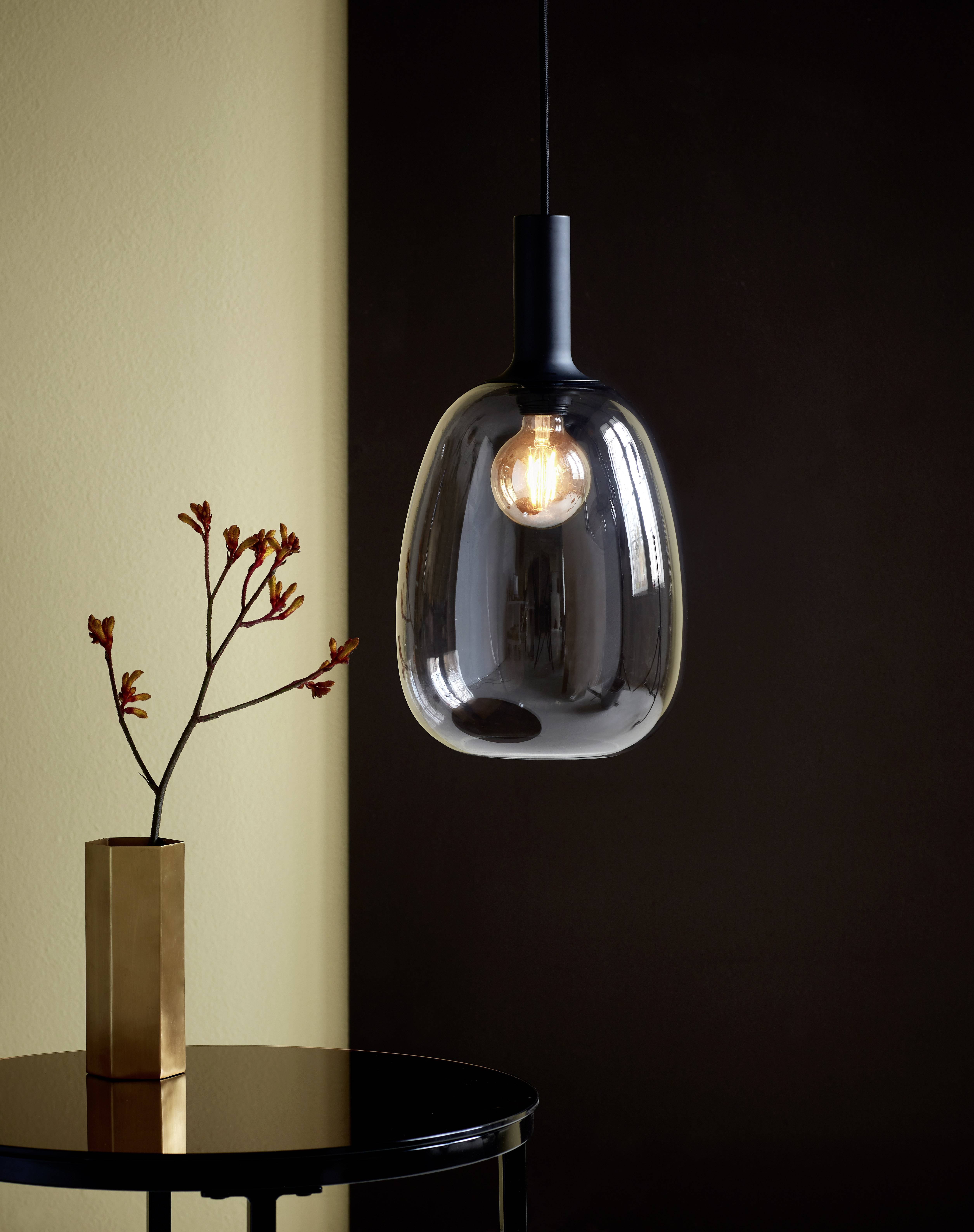 Suspension design au-dessus d'une table sombre avec une branche dépouillée dans un vase doré devant un mur brun.