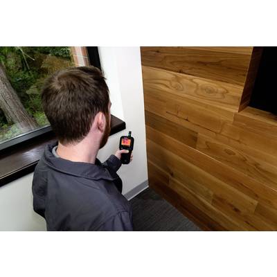 Un homme utilise un thermomètre infrarouge pour mesurer la température d'une section de mur en bois près d'une fenêtre.