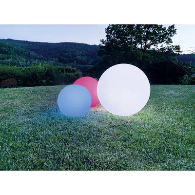 Trois boules lumineuses, deux blanches et une rouge, sont placées sur un champ herbeux devant un arrière-plan forestier au crépuscule.