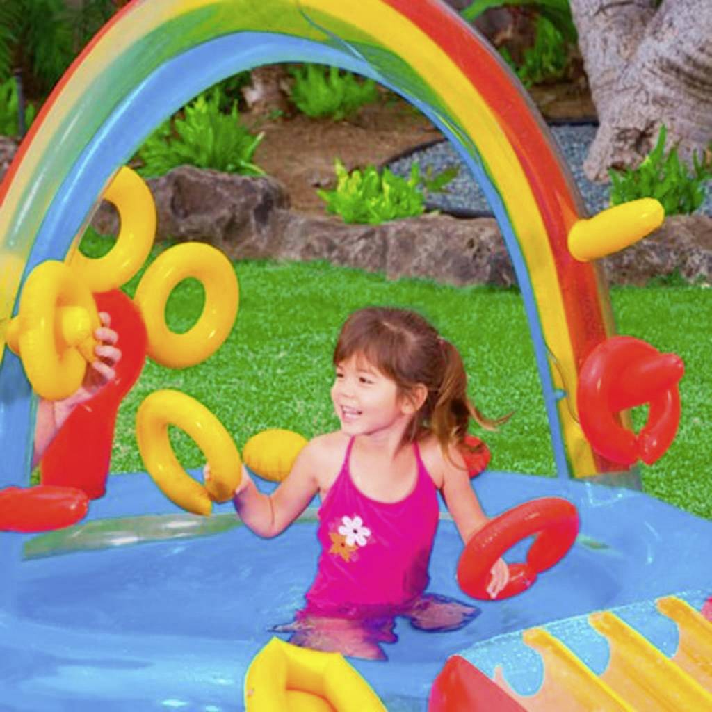 Un enfant joue joyeusement dans une aire de jeux aquatique colorée, avec des anneaux gonflables et une décoration arc-en-ciel en arrière-plan.