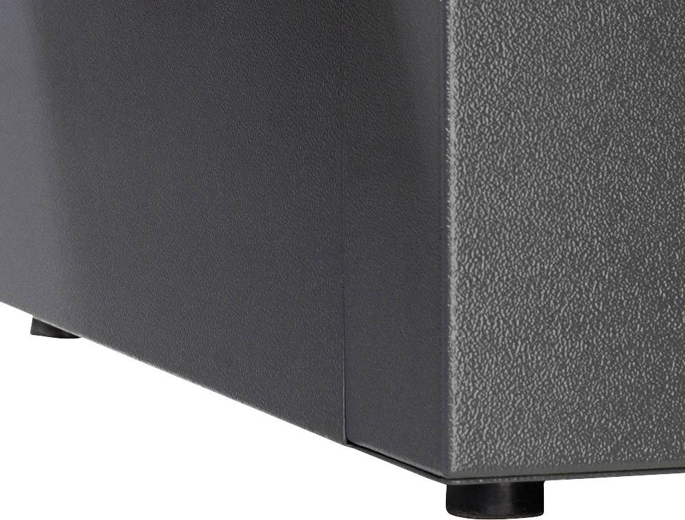 Un coin d'un appareil gris avec une surface structurée et des pieds noirs, probablement un haut-parleur ou un boîtier technique.