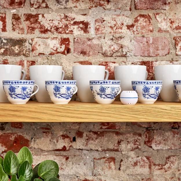 Une étagère en bois avec dix tasses à thé de style asiatique devant un mur de briques. Une plante se trouve au premier plan.