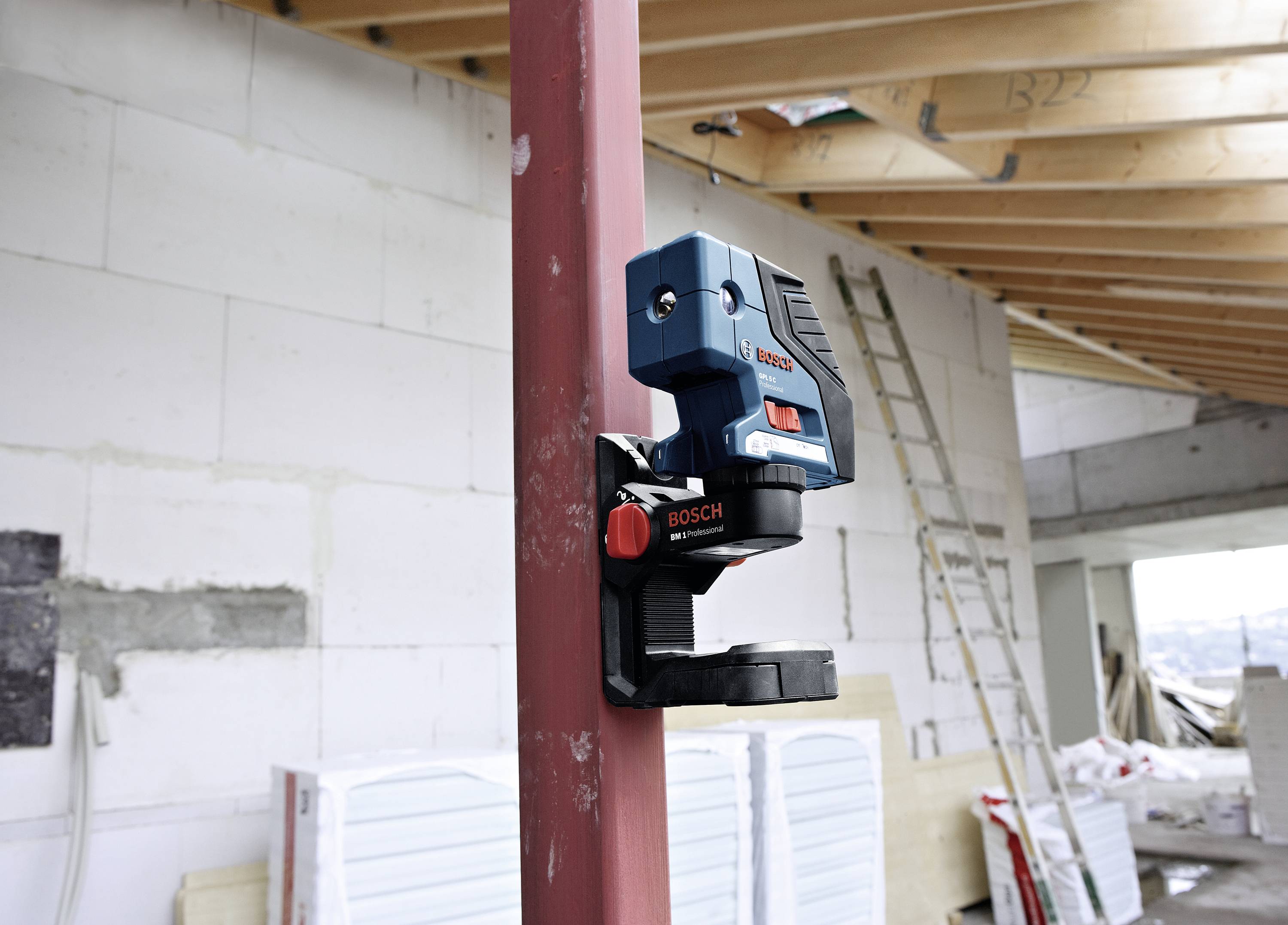 Un laser Bosch aligné sur un chantier, fixé à un poteau, entouré de matériaux de construction et d'une échelle en arrière-plan.