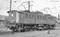 Une photographie historique montre une ancienne locomotive électrique sur une voie ferrée. Deux parties de la locomotive sont connectées entre elles.
