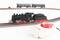 Un train miniature sur un rail, avec une locomotive noire et deux wagons verts en arrière-plan, à côté d'une unité de commande.