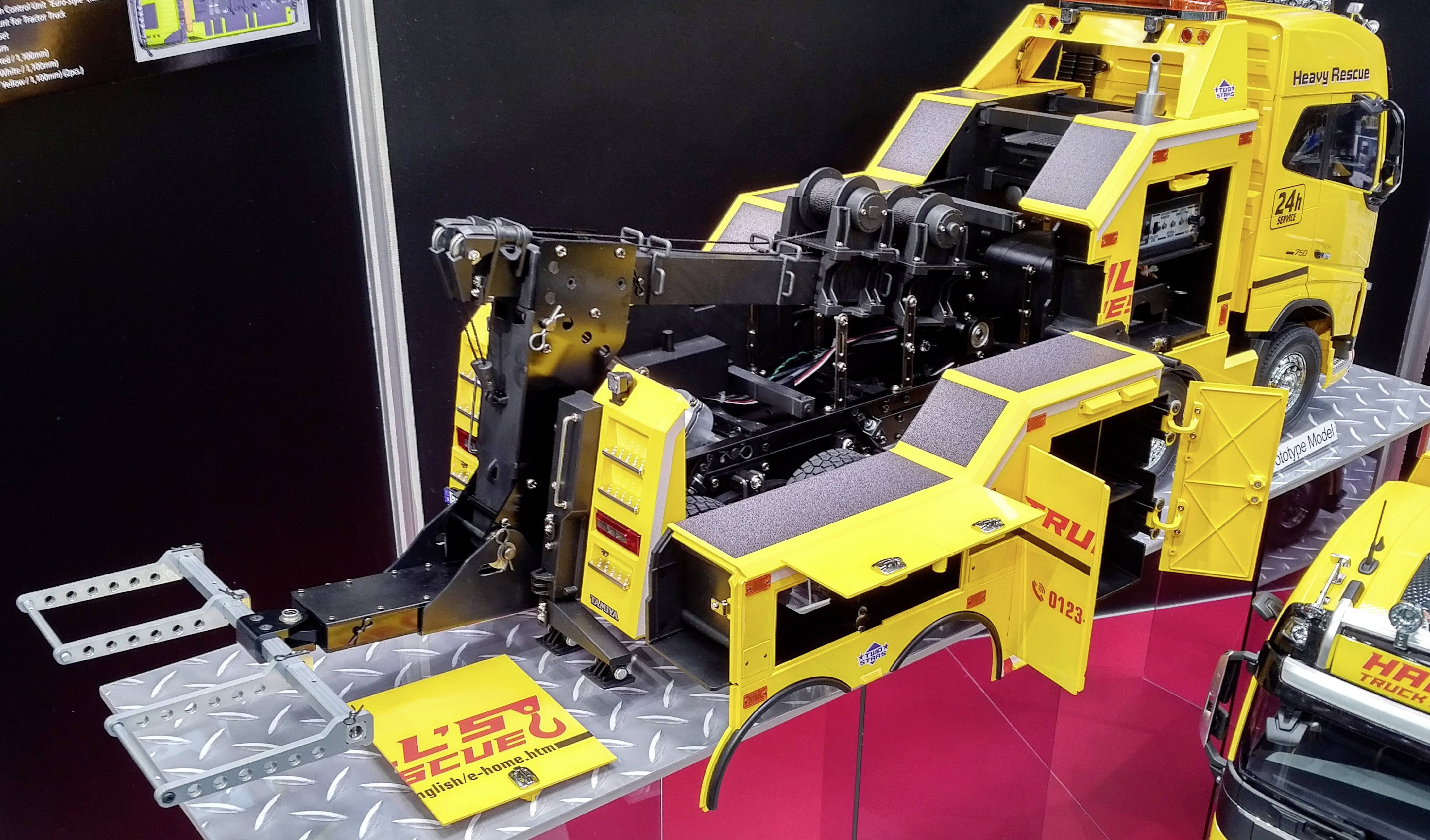 Modèle jaune d'un camion de dépannage poids lourds lors d'un salon. Le véhicule présente des inscriptions détaillées et des outils.