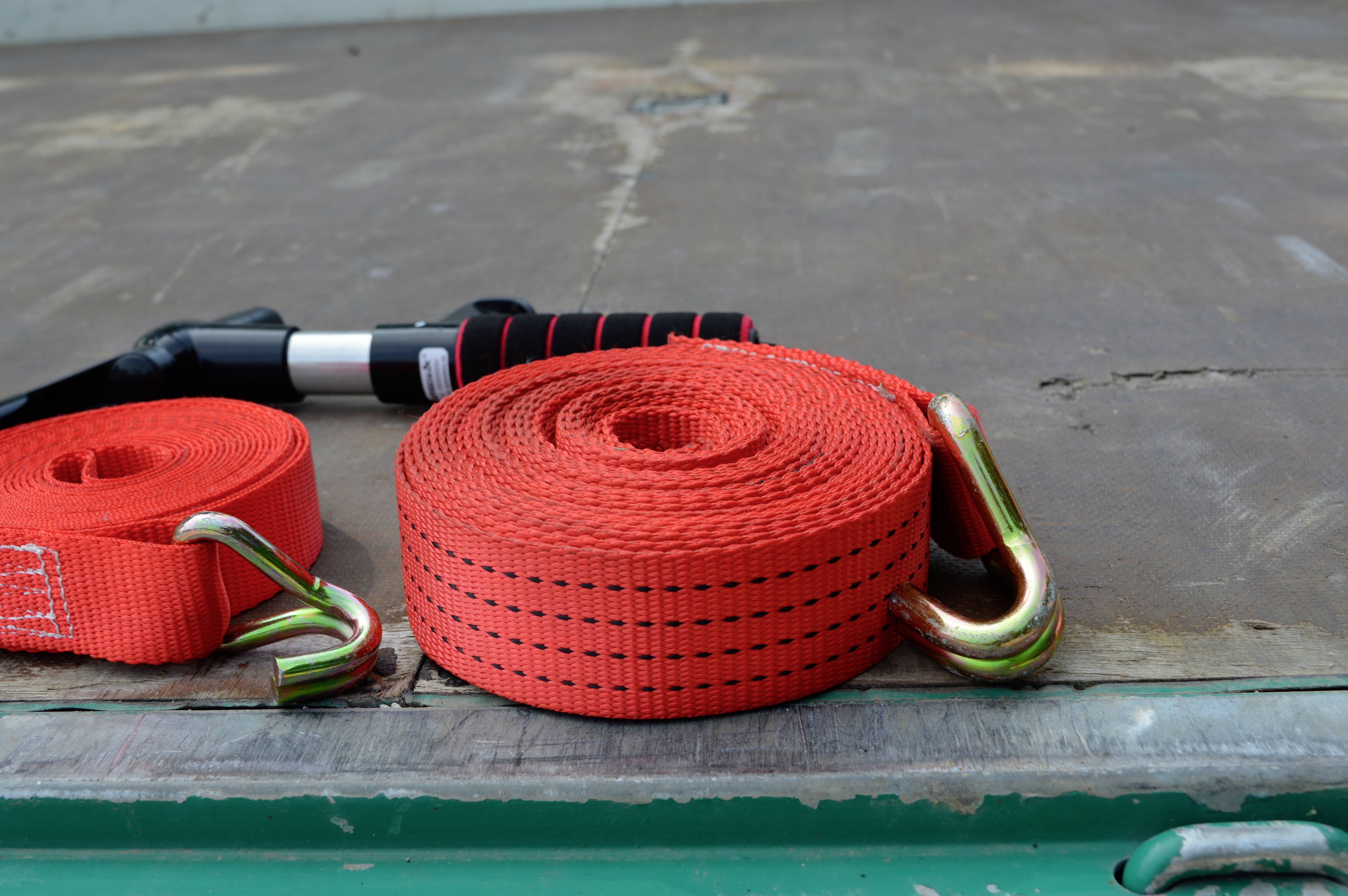 Sangles d'arrimage rouges avec crochets sur un support en bois. À l'arrière-plan, un levier noir avec une poignée rouge.
