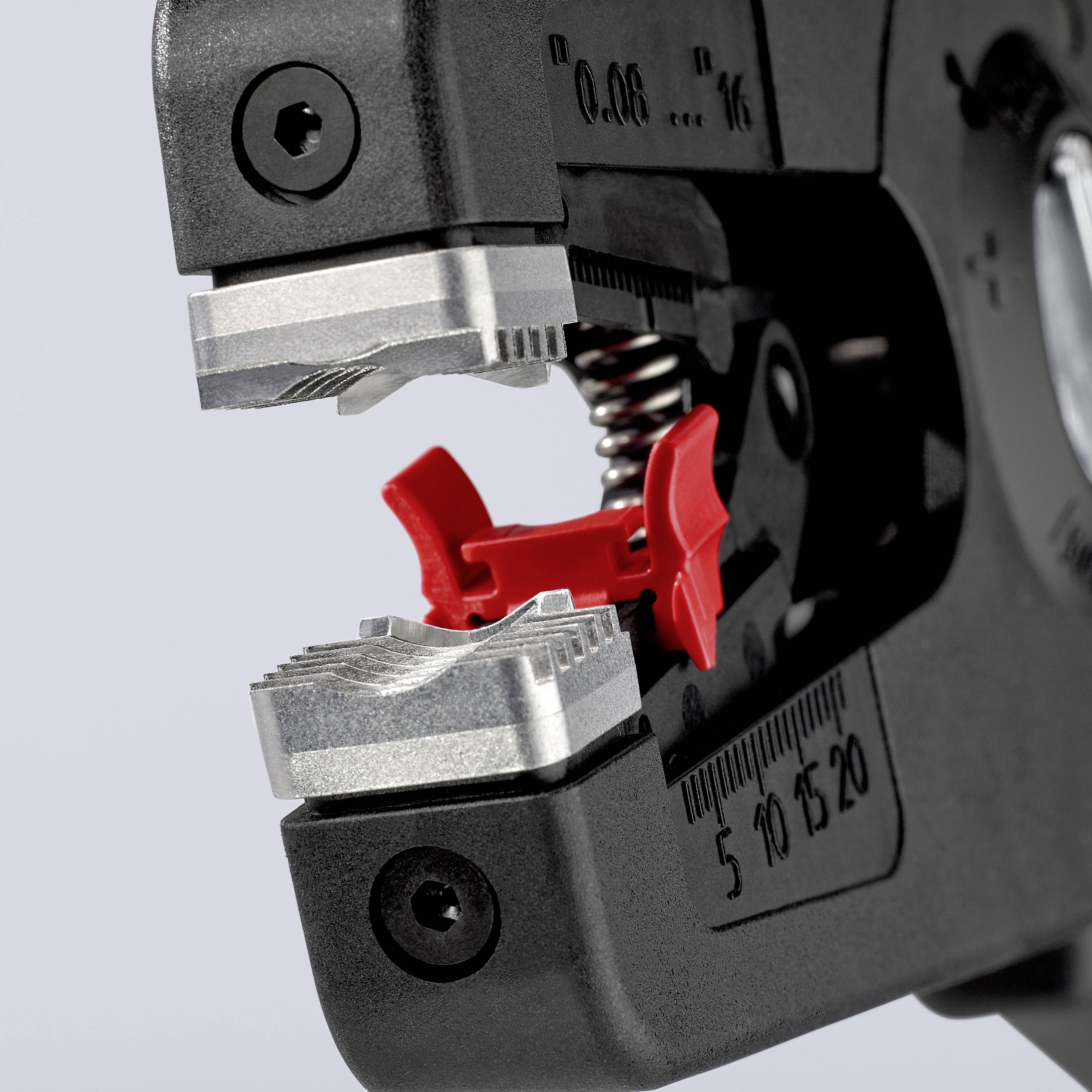 Gros plan d'une pince à câbles dont les mâchoires métalliques maintiennent une pièce en plastique rouge. L'échelle affiche des valeurs de mesure.