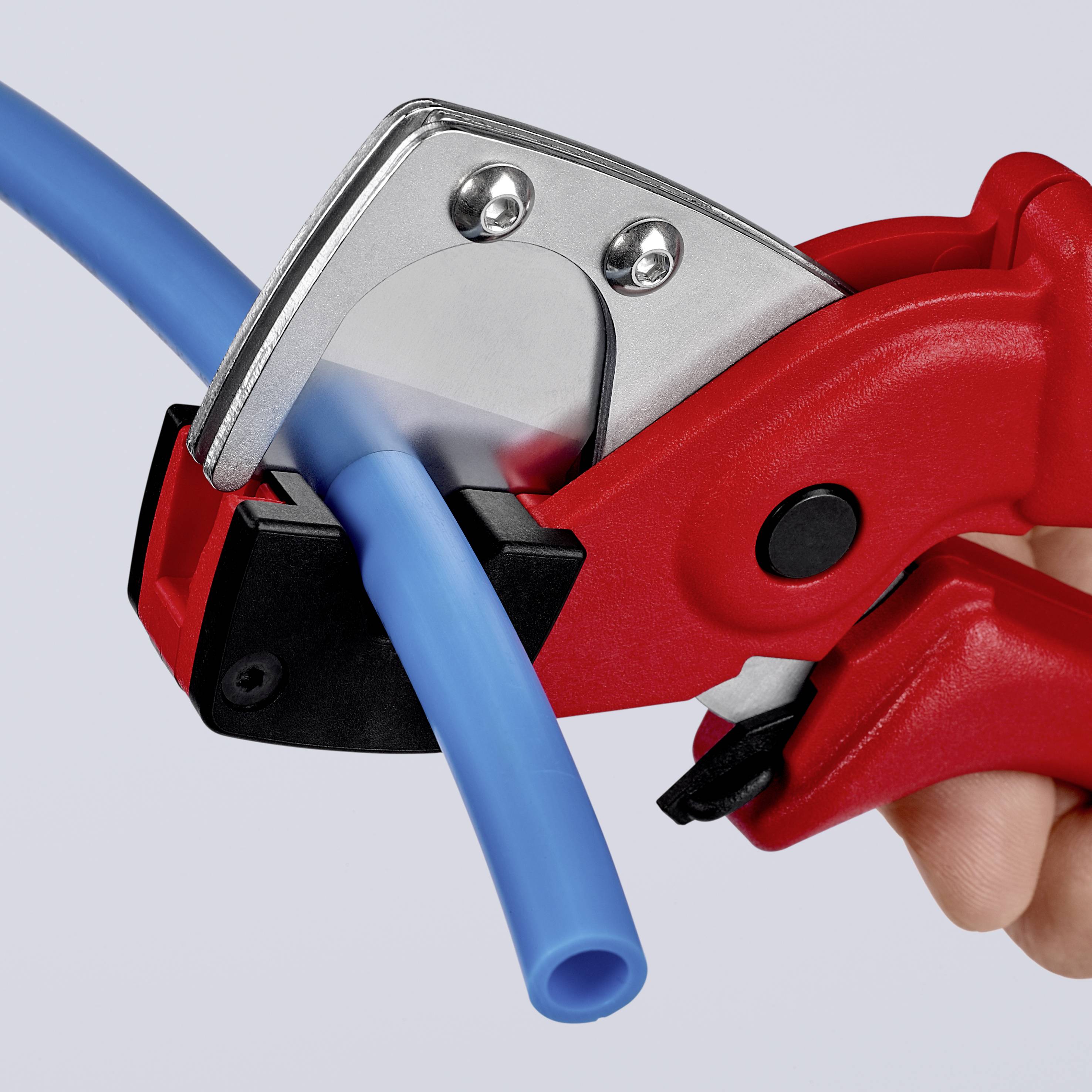 Une main coupe un tuyau bleu avec un coupe-tube rouge, gros plan.