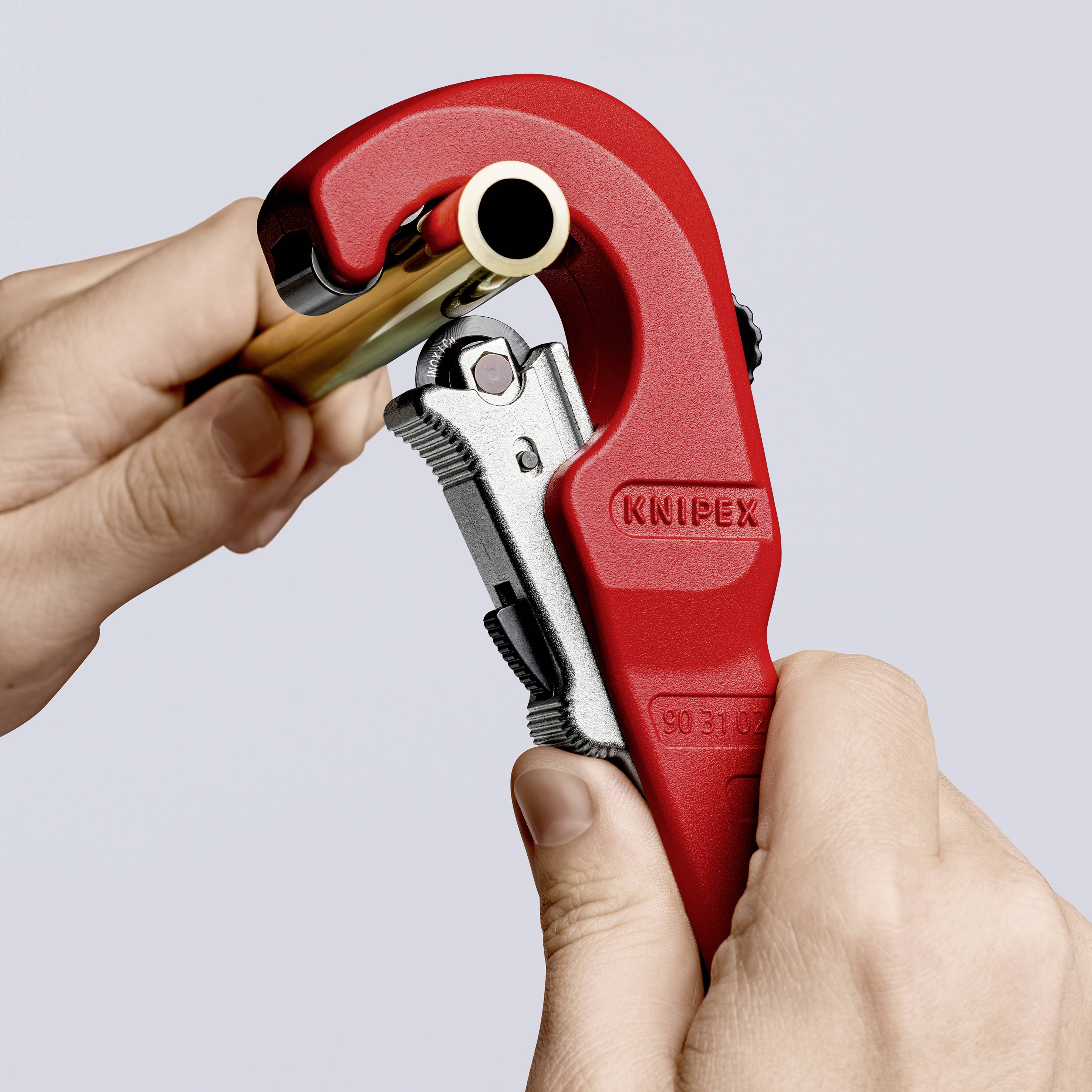 Une personne coupe un tube à l'aide d'un coupe-tube rouge. L'outil porte l'inscription 'Knipex'.