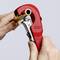 Une personne coupe un tube à l'aide d'un coupe-tube rouge. L'outil porte l'inscription 'Knipex'.