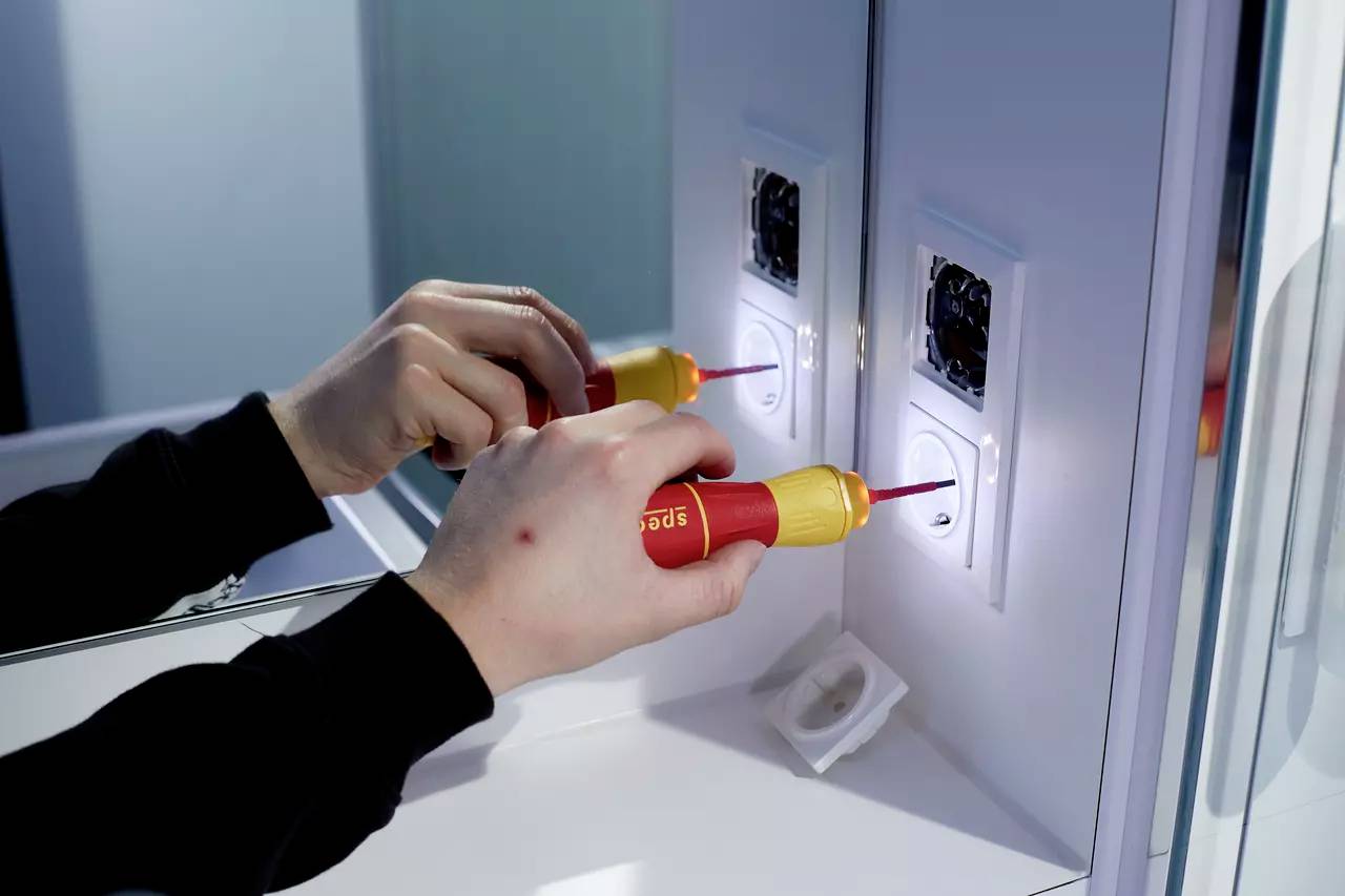 Personne installant une prise électrique sur un mur avec un tournevis isolé, qui est utilisé dans un espace restreint.