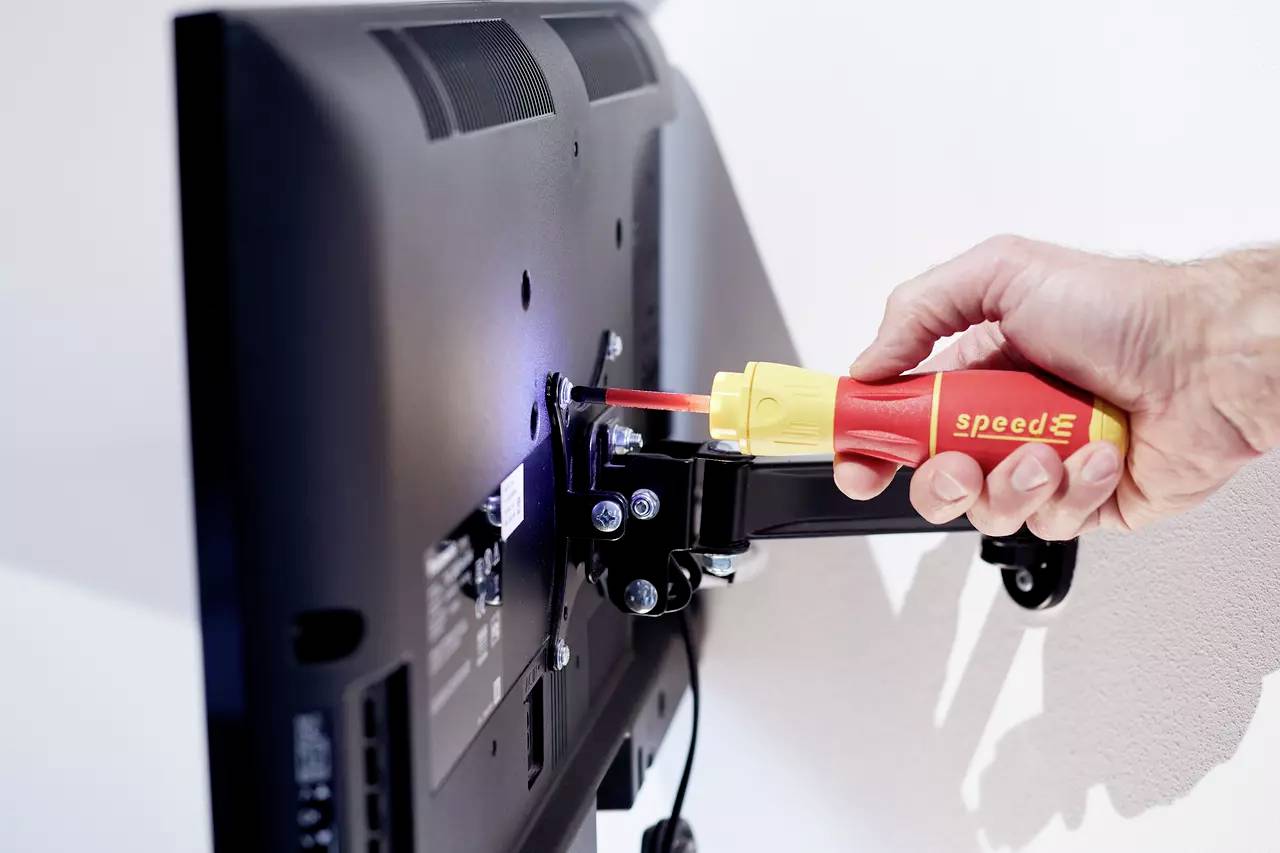 Une main resserre la vis sur le support d'un moniteur fixé au mur à l'aide d'un tournevis.