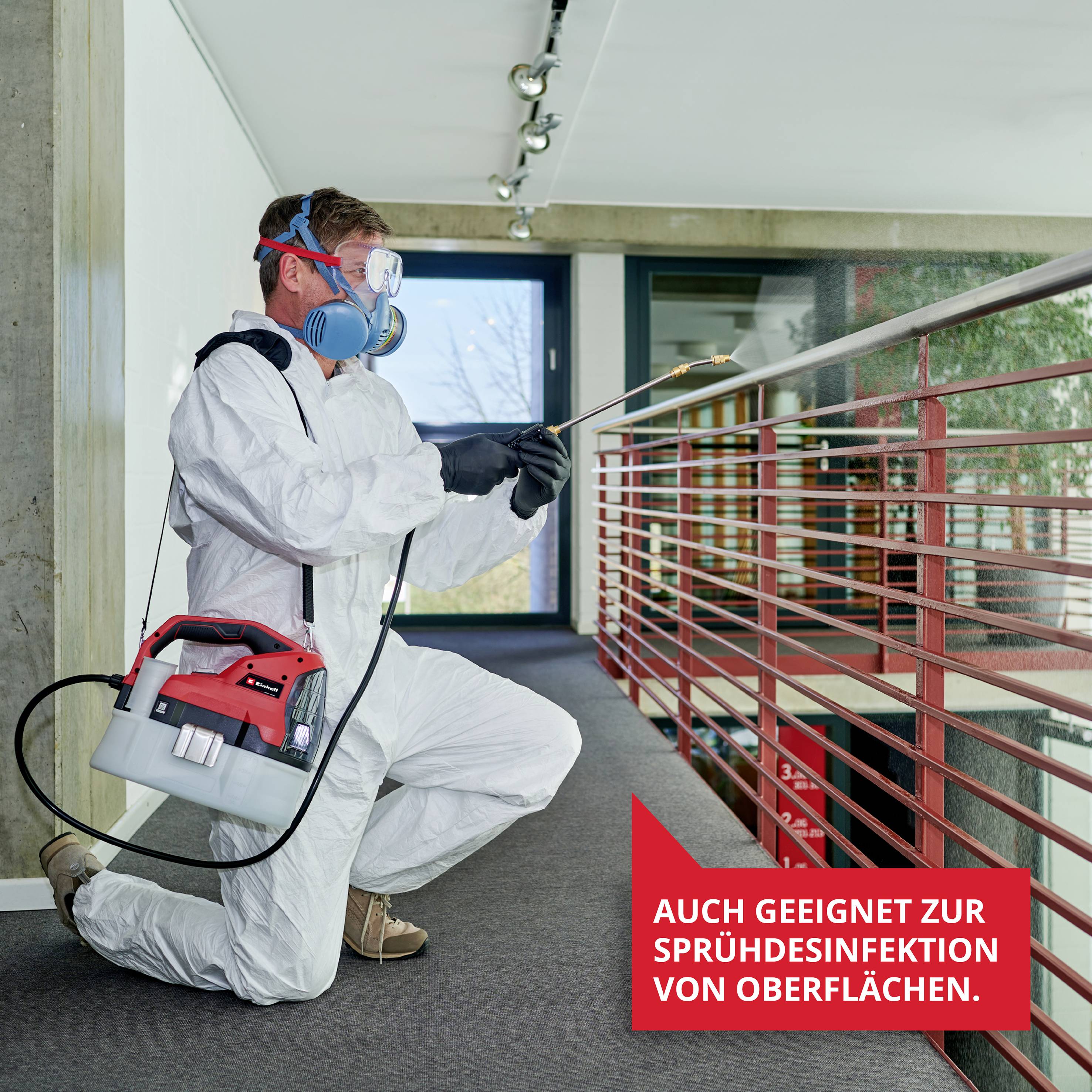 Personne en combinaison de protection et masque respiratoire désinfectant une rampe avec un appareil de pulvérisation ; légende : 'Également adapté à la désinfection par pulvérisation des surfaces.'