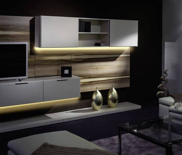 Salon avec un mur de meuble suspendu moderne au look bois. Éclairage LED, deux vases dorés, table basse en verre et arrière-plan noir.