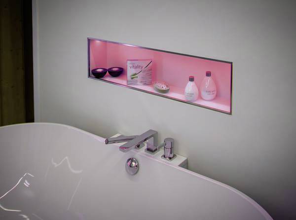 Espace de salle de bain moderne avec une baignoire blanche autoportante. Une niche murale éclairée présente des produits de soin.