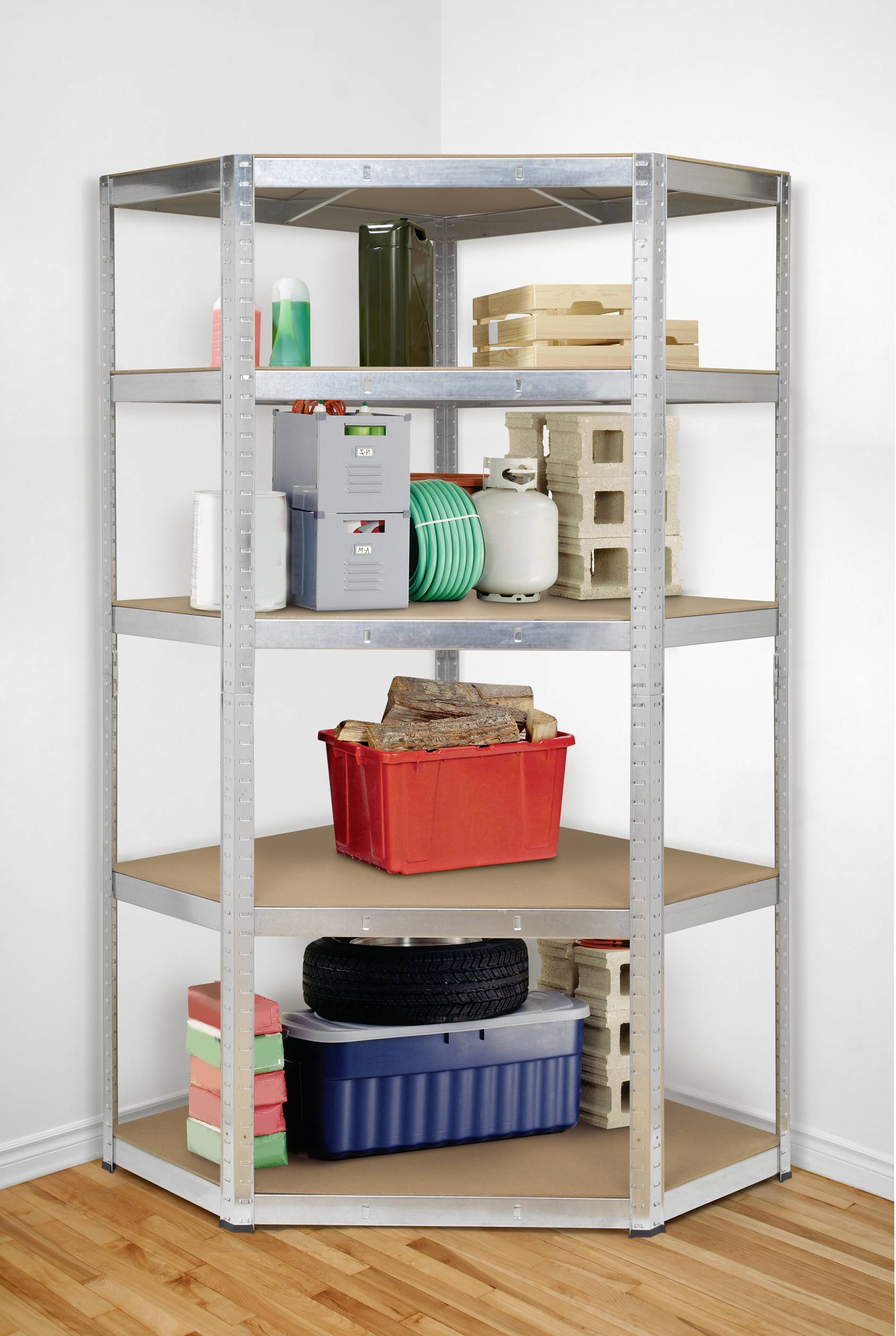 Étagère métallique dans un coin, remplie d'objets divers : cartons, bouteilles, jouets, pneus et un coffre rouge contenant du bois.