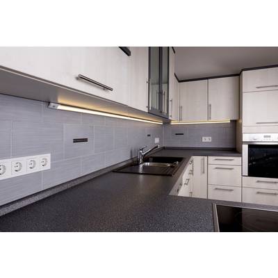 Cuisine moderne avec évier d'angle, plan de travail gris et éclairage sous-jacent. Des meubles hauts blancs et une plaque de cuisson intégrée sont visibles.