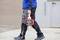 Une personne portant une veste bleue et un pantalon noir marche sur un sol pavé en transportant une balance électronique rouge pour grue.