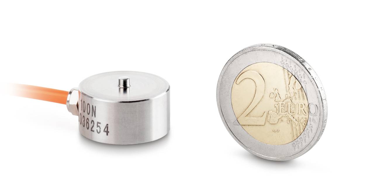 Petit capteur rond à côté d'une pièce de 2 euros pour comparer la taille. Le capteur est en métal avec une connexion par câble.