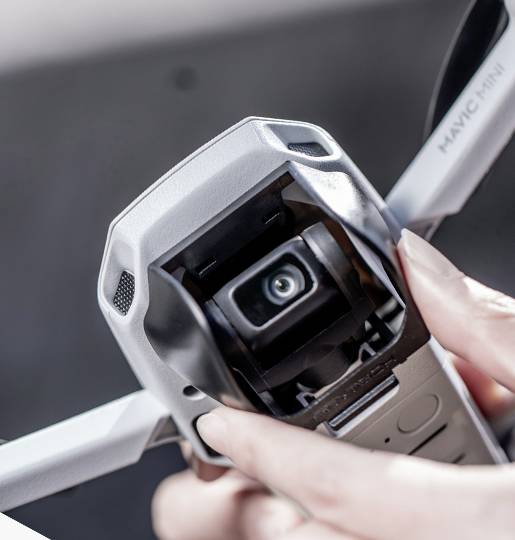 'Gros plan d'une main tenant un drone. La mise au point est sur la caméra du drone, utilisée pour les prises de vue aériennes.'