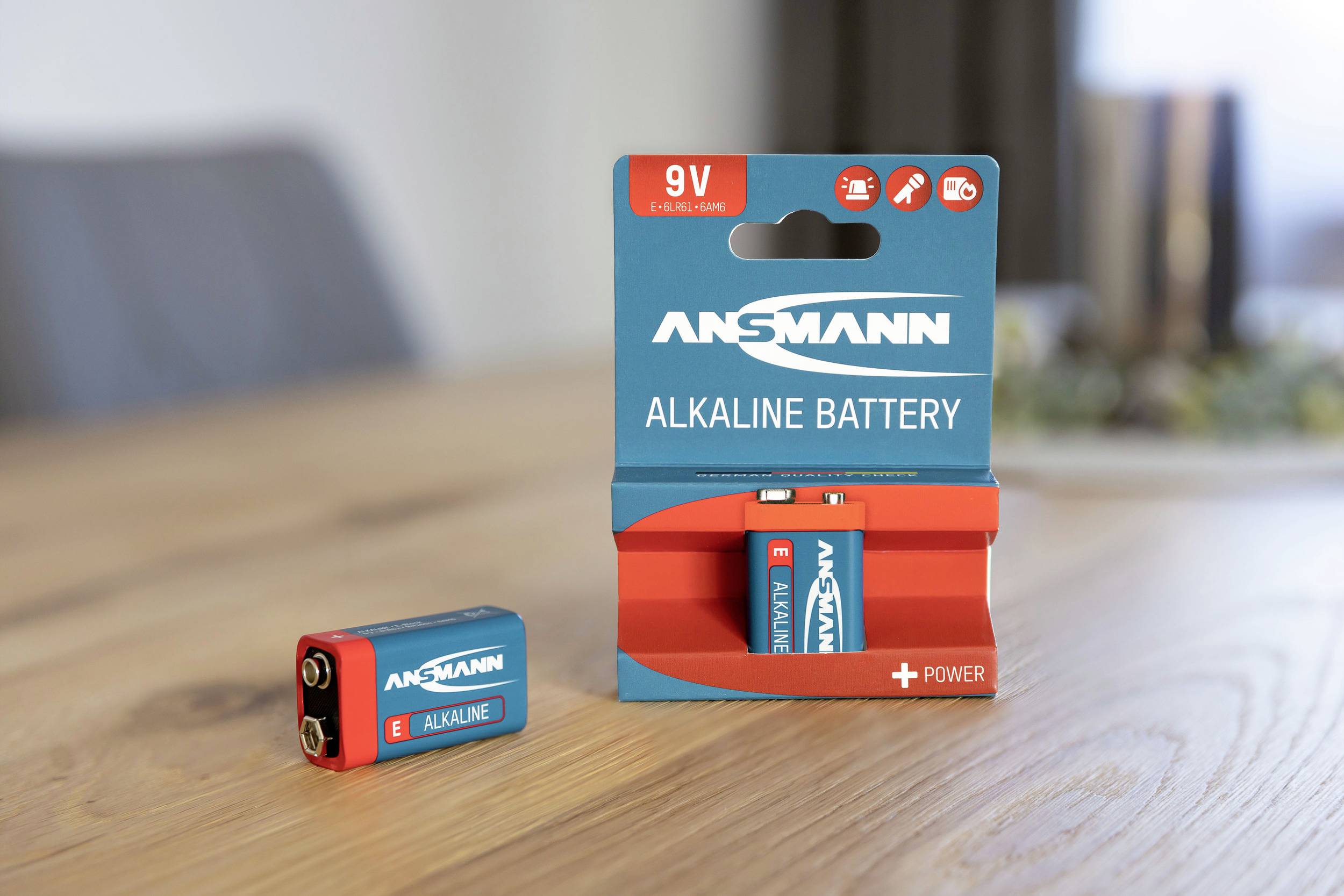 Une pile alcaline Ansmann 9V est posée à côté de son emballage sur une table en bois.