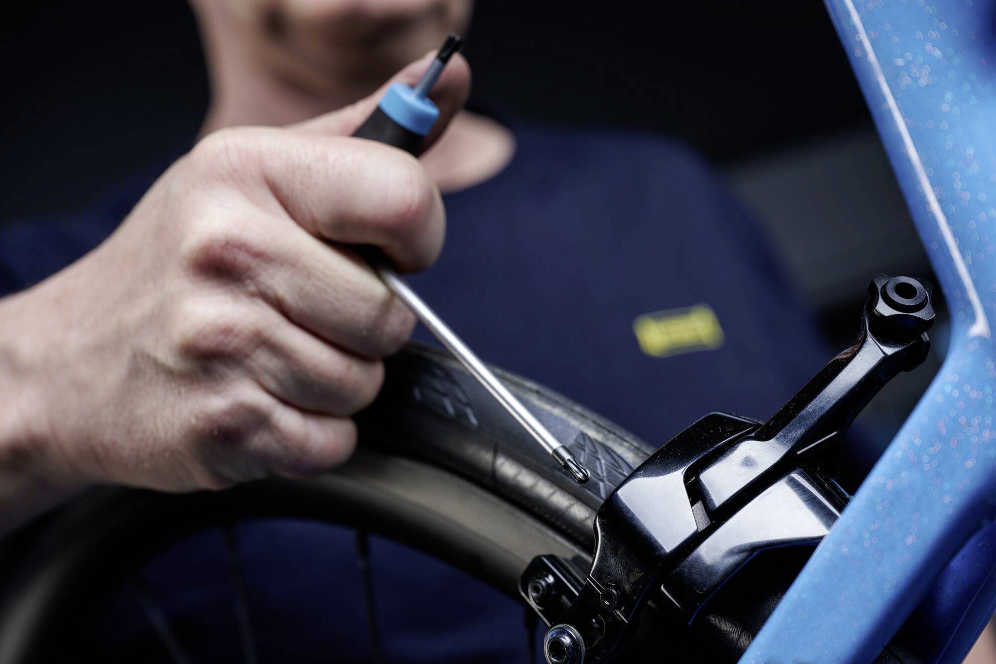 Une personne répare un pneu de vélo en vérifiant une valve avec un outil. Le focus est mis sur la main et l'outil.