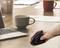 Une main tient une souris verticale ergonomique sur une table d'ordinateur portable avec des tasses à café en arrière-plan, symbolisant un travail confortable.