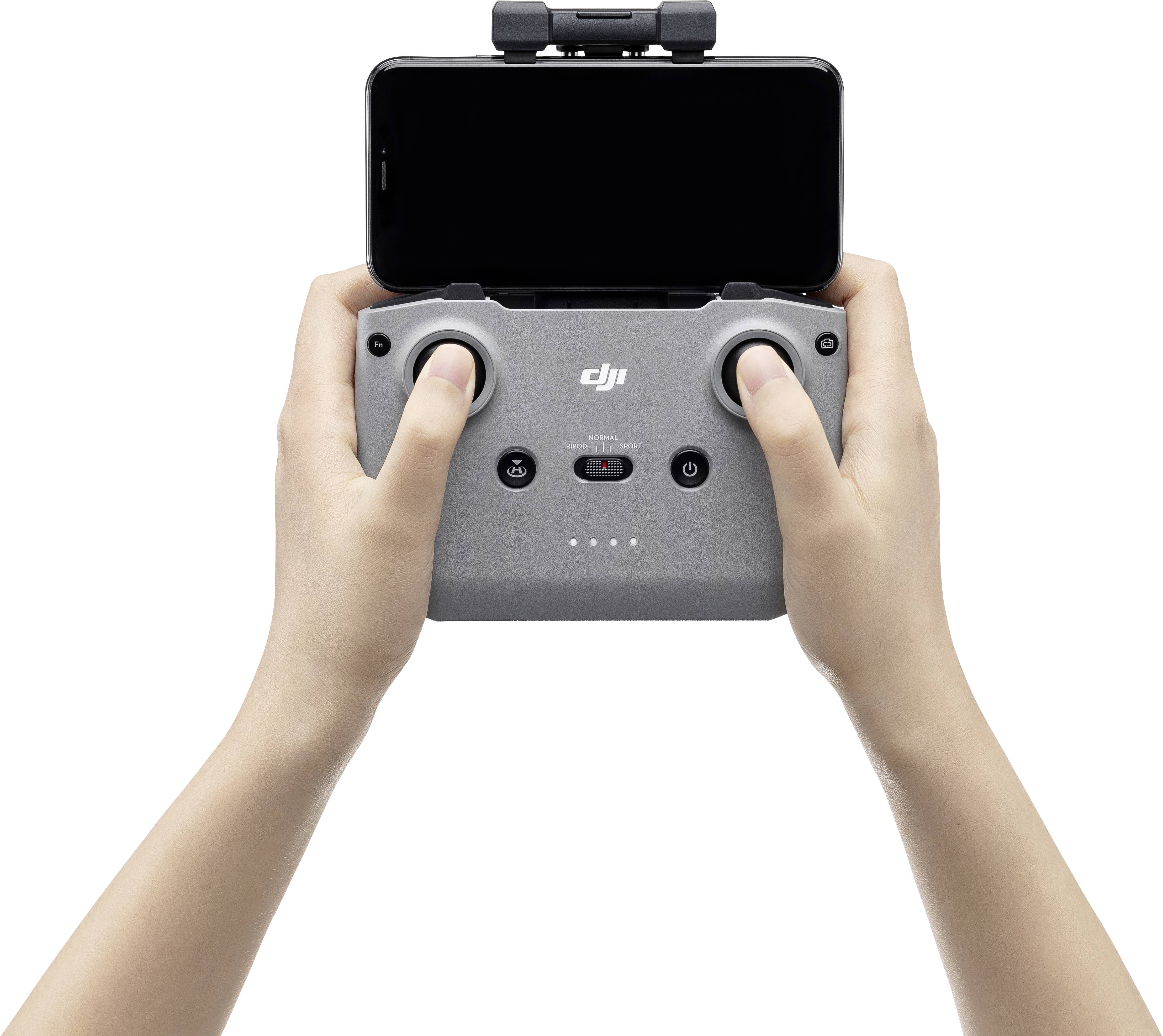 Une personne tient une télécommande de drone avec ses deux mains. Un smartphone est fixé au-dessus.