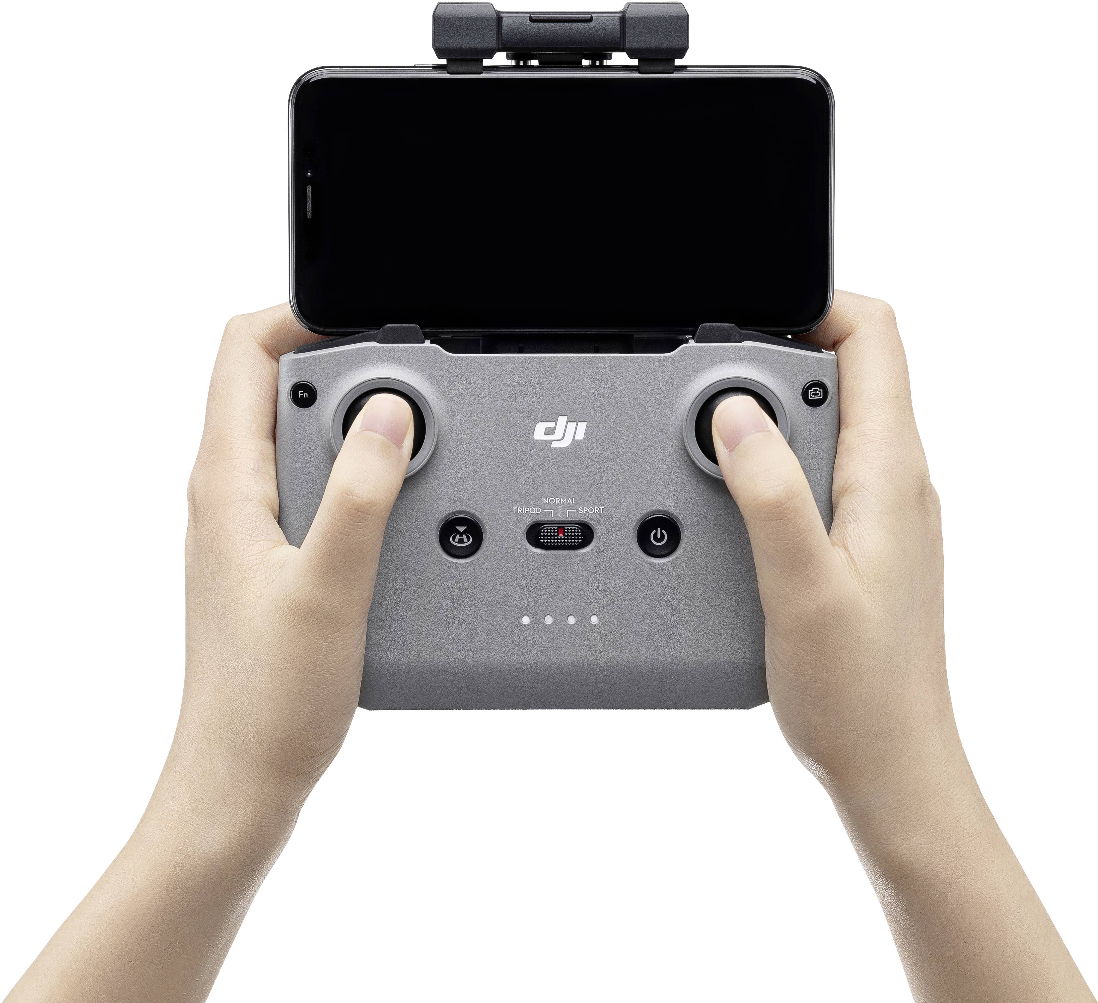 Deux mains tiennent une télécommande grise avec un smartphone monté, utilisée pour piloter des drones.