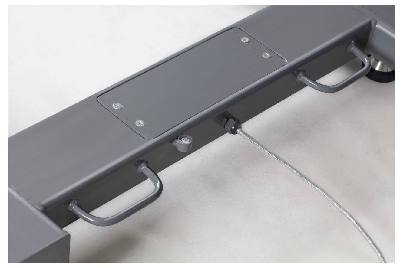 Une pièce métallique grise avec plusieurs poignées et un couvercle fixé par des vis. Un câble est attaché sur le côté.