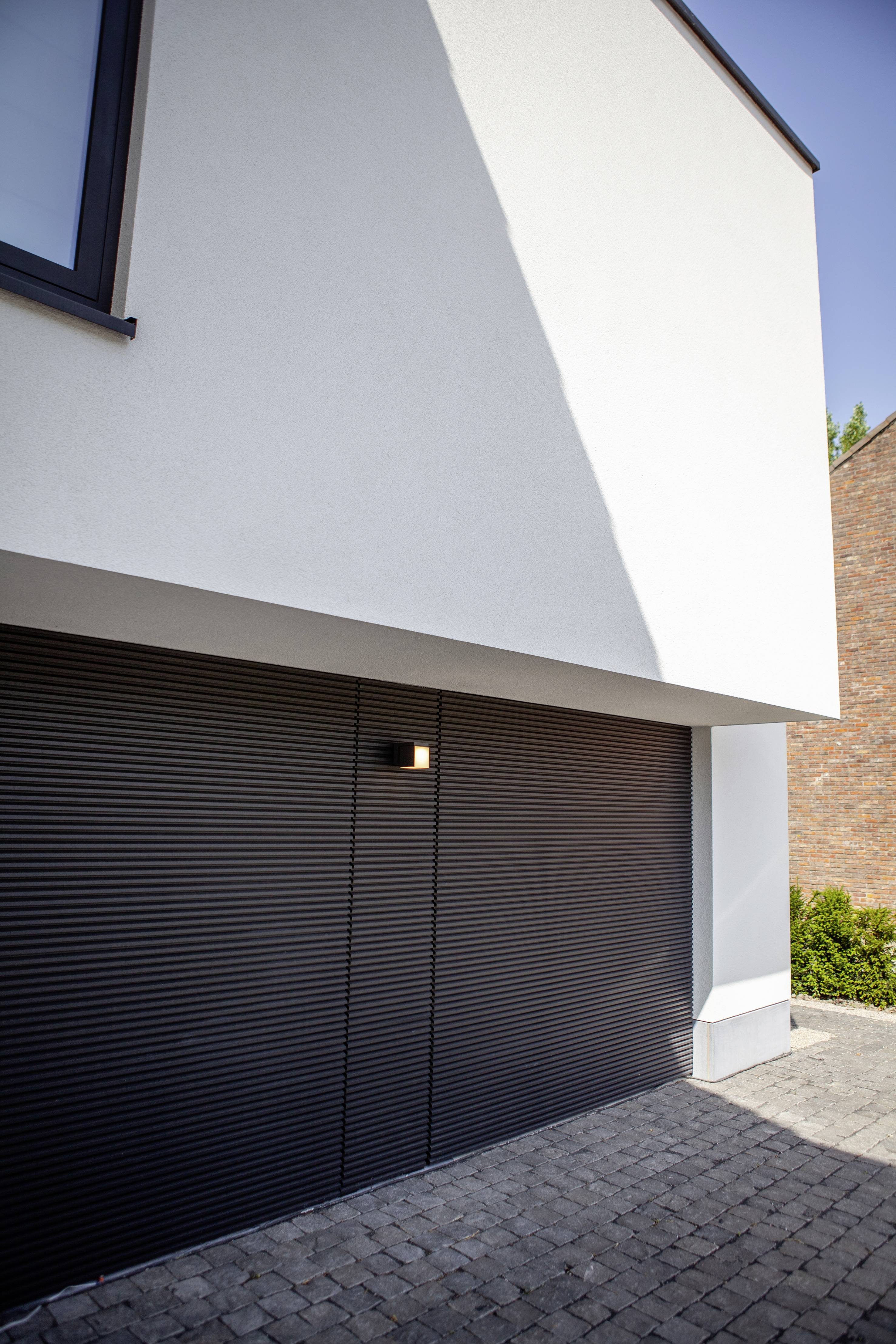 Façade d'une maison avec une porte de garage fermée et noire, architecture moderne, jour ensoleillé, allée pavée.
