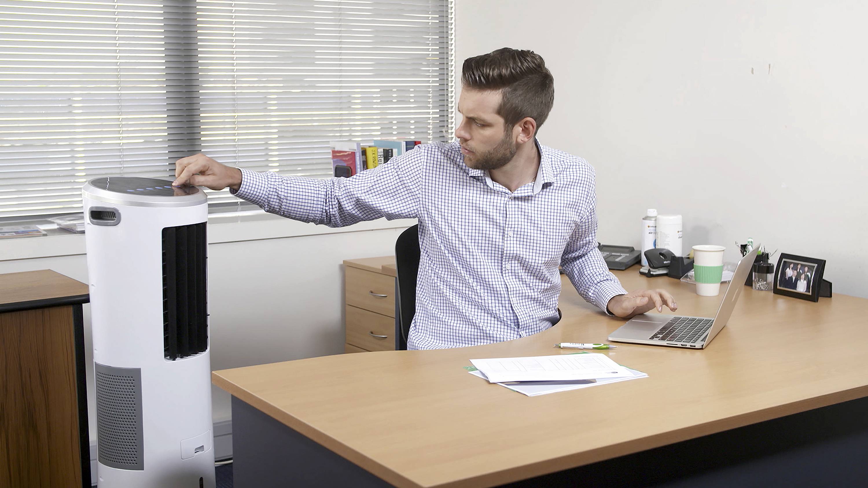 Un homme est assis à un bureau et règle les paramètres d'un purificateur d'air. Un ordinateur portable et des documents sont disposés devant lui.