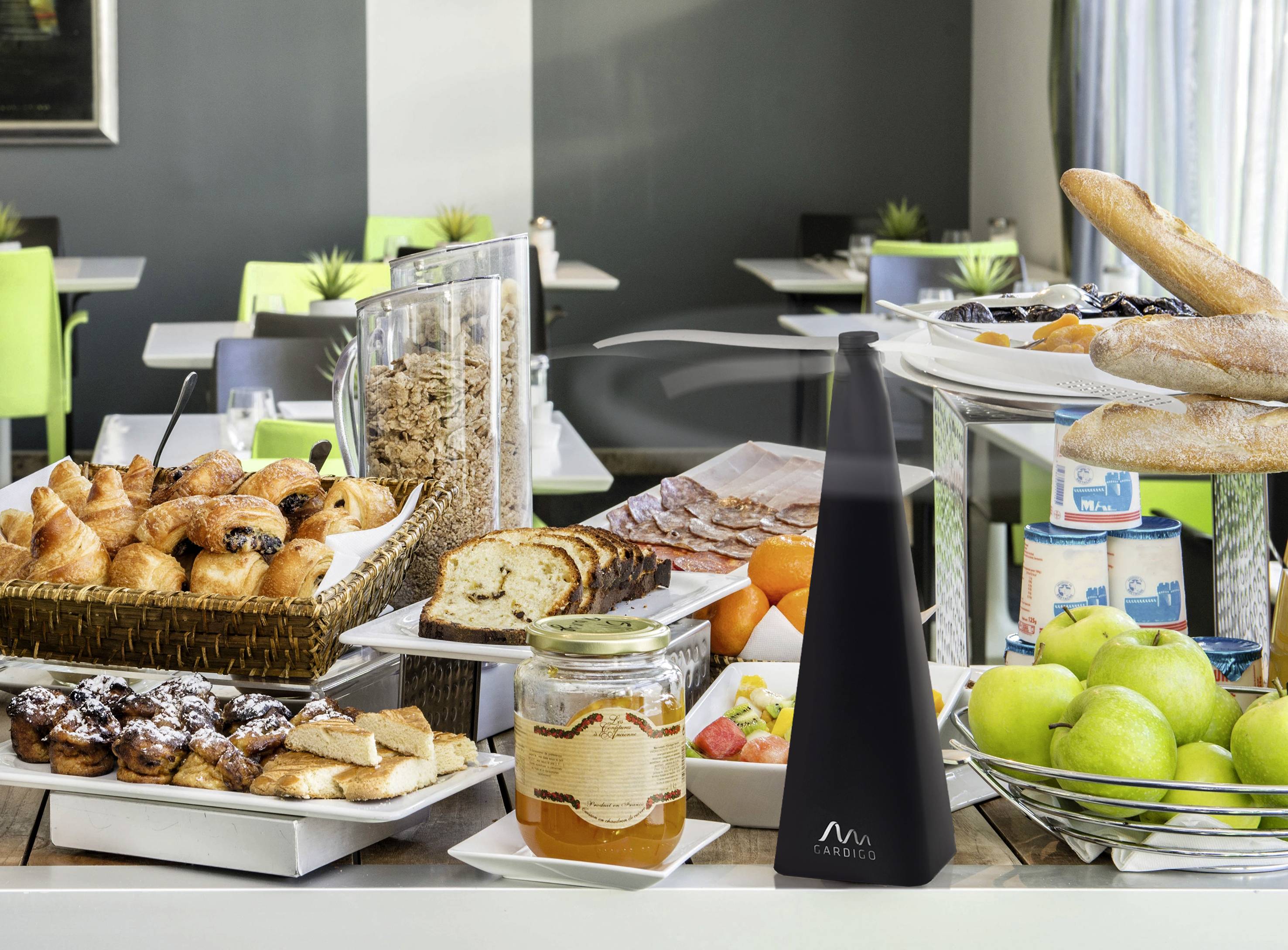 Un buffet de petit-déjeuner avec des croissants, du pain, de la confiture, des fruits, du yaourt et des verres de muesli sur une table dans un espace repas moderne.