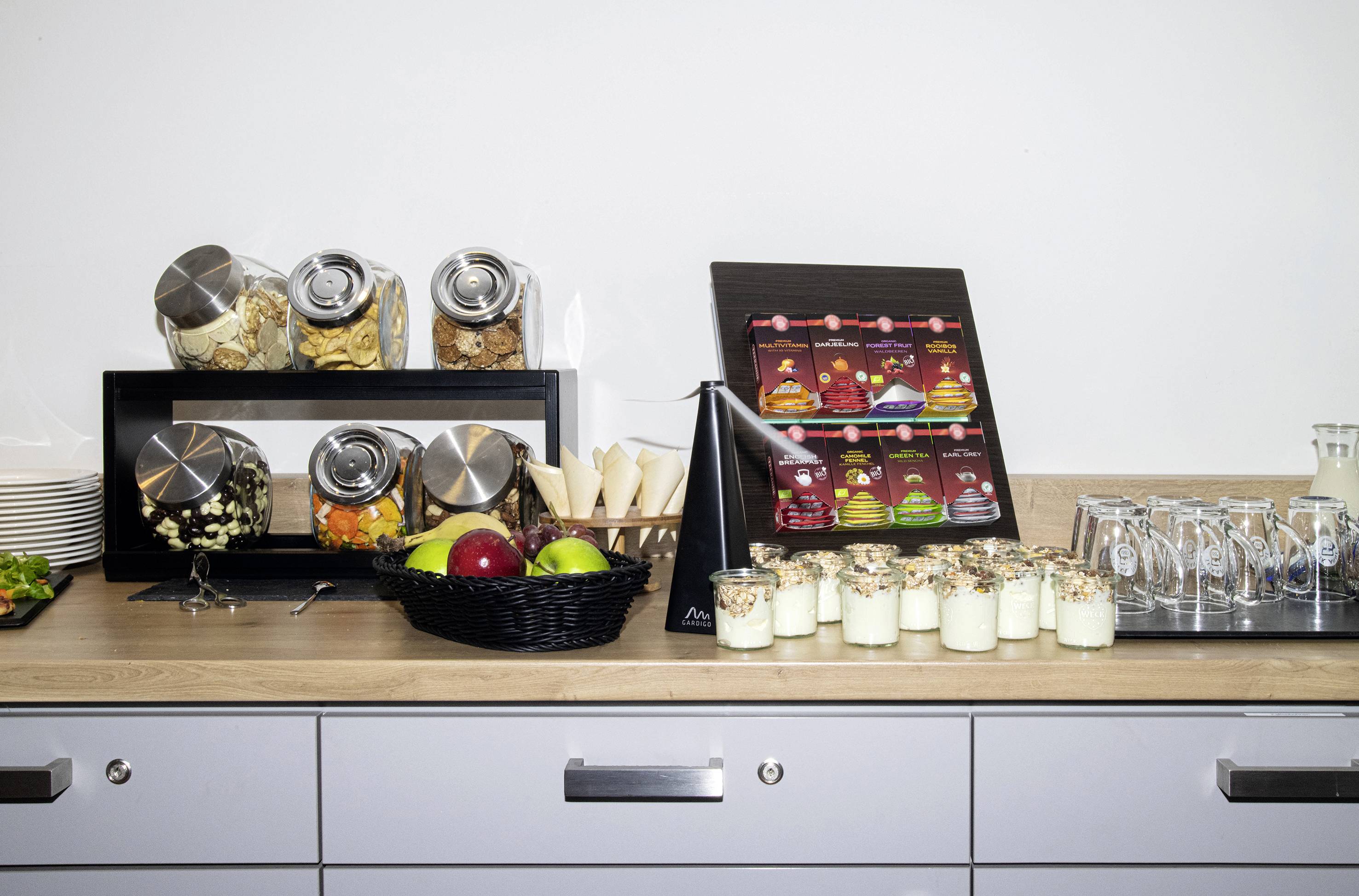 Un buffet avec des müeslis dans des bocaux, des fruits frais dans un panier, du yaourt avec des müeslis et des verres frais. Idéal pour le petit-déjeuner.