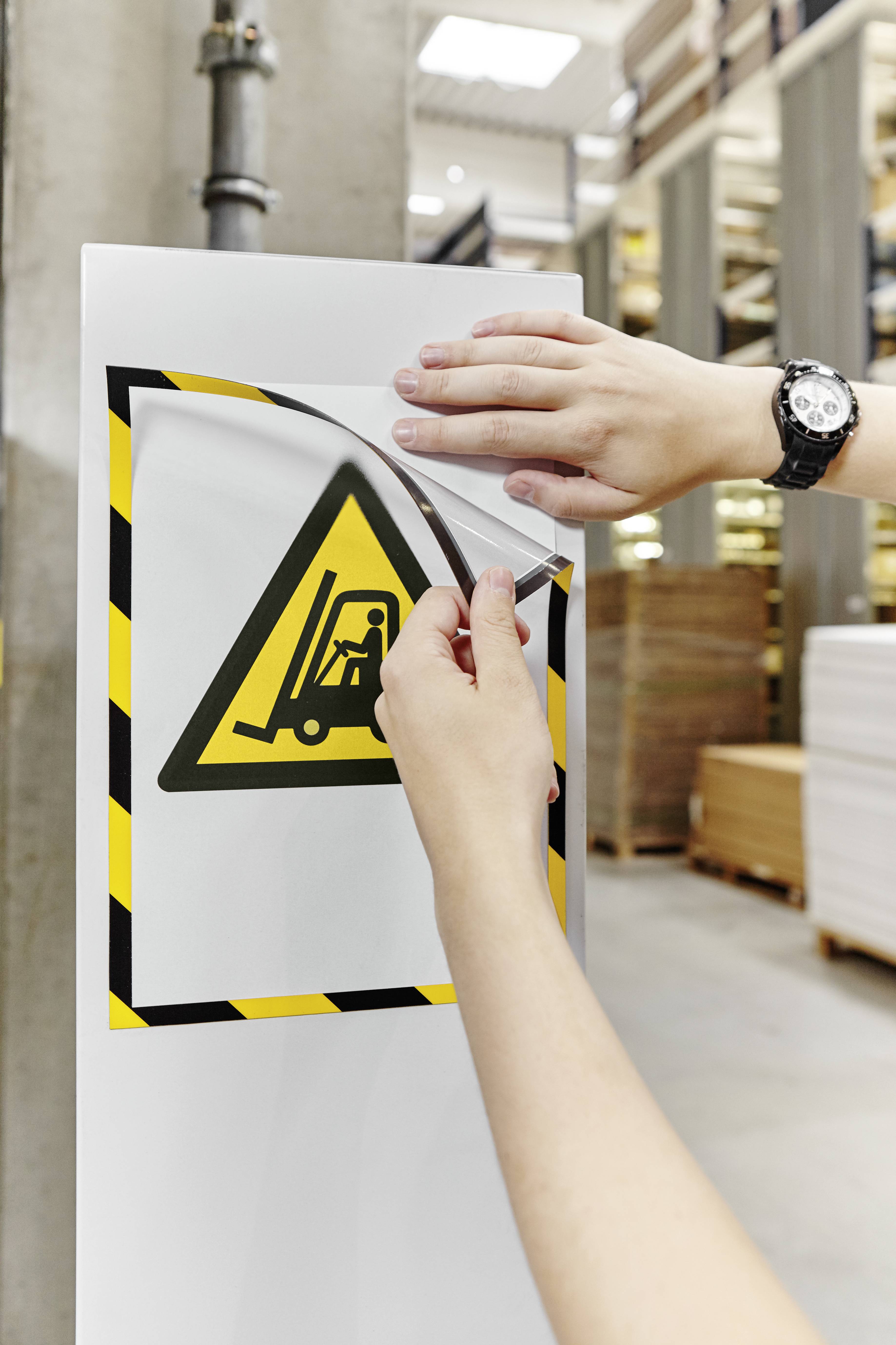 Une personne retire un panneau d'avertissement indiquant une zone de danger de chariot élévateur d'une surface claire dans un entrepôt.